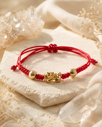 Red string Pixiu bracelet displayed on a stone tray in warm natural light